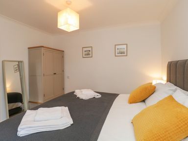 A bedroom with a bed with yellow pillows towels on the bed wardrobe mirror and framed pictures on the wall at The Postmasters House in Windermere