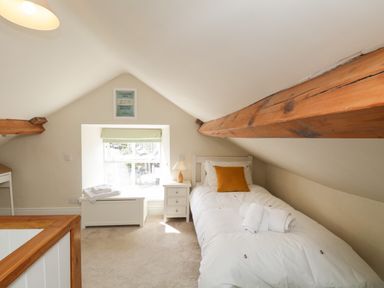 A bedroom with a single bed bedside table chest under window and exposed wooden beams at The Postmasters House in Windermere
