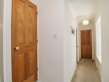 A narrow hallway with beige carpet two wooden doors white walls a framed picture and a pendant light at The Postmasters House in Windermere