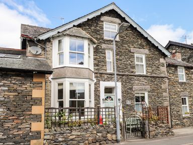 Stone house with bay windows white door and small garden fenced by a stone wall at The Postmasters House in Windermere
