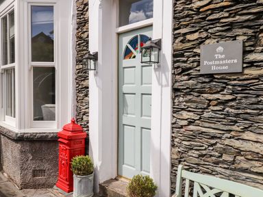 Front entrance with light green door red mailbox stone wall and two potted plants at The Postmasters House in Windermere
