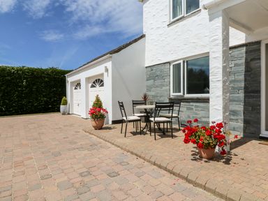 An outdoor patio area with a table and four chairs and flower pots near a white house with a double garage at Trevore Farmhouse in Chacewater
