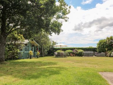 A garden with a green shed large tree patio table with umbrella and outdoor seating area with hot tub at Trevore Farmhouse in Chacewater