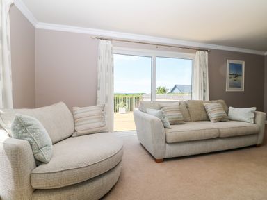A living room with two beige sofas and a large window with curtains at Trevore Farmhouse in Chacewater