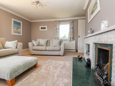 A living room with beige sofas a light blue ottoman and a fireplace at Trevore Farmhouse in Chacewater