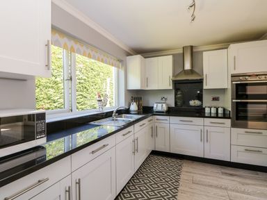 A kitchen with white cabinets black countertops a stainless steel sink a microwave oven and a patterned rug on the floor at Trevore Farmhouse Chacewater