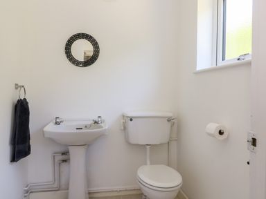 A bathroom with a pedestal sink a toilet a round mirror a towel and a window at Trevore Farmhouse in Chacewater