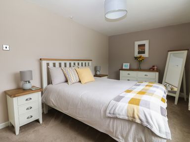 A bedroom with a bed pillows bedside tables lamps a dresser flowers and a standing mirror at Trevore Farmhouse in Chacewater