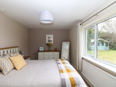 A bedroom with a bed a dresser and a window showing a garden at Trevore Farmhouse in Chacewater