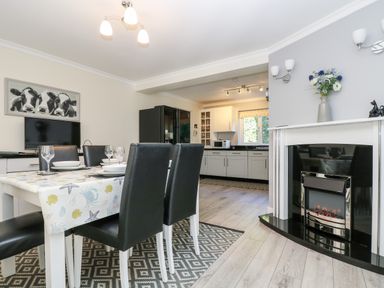 A dining area with a table set for four black chairs and a connected kitchen with white cabinets and a fireplace at Trevore Farmhouse in Chacewater