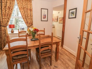 A dining room with a wooden table and chairs with flowers on the table and a window with curtains at Manod View in Blaenau Ffestiniog