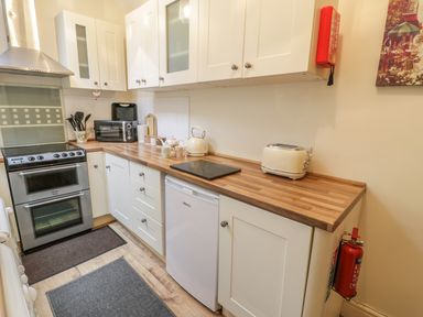 A kitchen with white cabinets wooden countertops a stove microwave kettle and toaster and a fire extinguisher on the wall at Manod View in Blaenau Ffestiniog