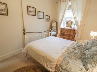 A bedroom with a bed a wooden dresser a standing mirror framed pictures on the wall and curtains on a window at Manod View in Blaenau Ffestiniog