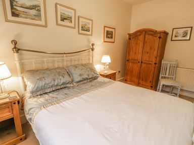 A bedroom with a bed framed by a metal headboard bedside tables lamps a wooden wardrobe a chair and framed pictures on the wall at Manod View in Blaenau Ffestiniog