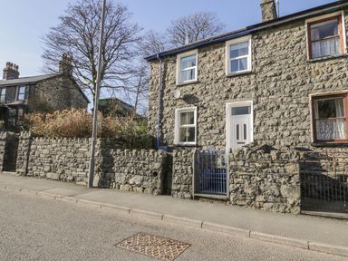 A stone house with white door and windows and a blue metal gate by a stone wall on a street at Manod View in Blaenau Ffestiniog