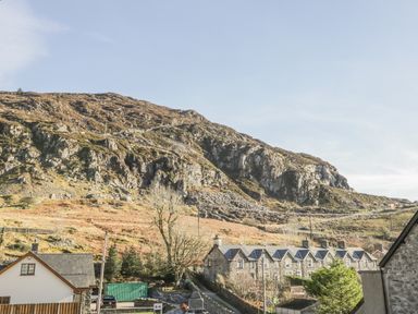 Rocky hillside behind a row of stone houses and a white house with a fenced yard at Manod View in Blaenau Ffestiniog