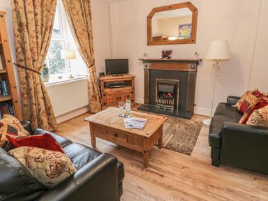 A living room with two leather sofas a wooden coffee table a fireplace and floral curtains at Manod View in Blaenau Ffestiniog