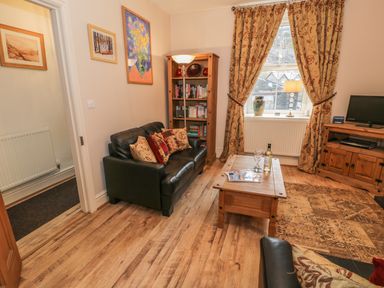 A living room with leather sofas, a wooden coffee table, bookshelf, TV stand, patterned curtains, and framed paintings at Manod View in Blaenau Ffestiniog