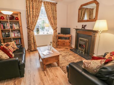 A living room with black leather sofas a wooden coffee table a fireplace and bookshelves at Manod View in Blaenau Ffestiniog