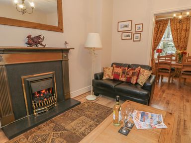 A living room with a fireplace black leather sofa and coffee table next to a dining room at Manod View in Blaenau Ffestiniog