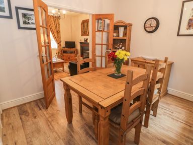 A dining room with a wooden table and chairs and a vase of flowers at Manod View in Blaenau Ffestiniog