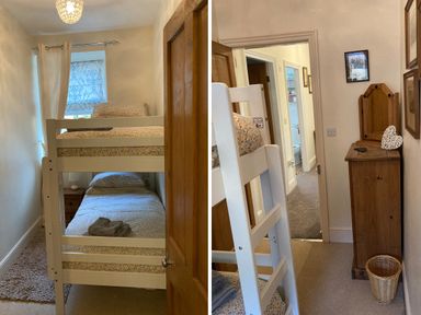 A bedroom with white bunk beds and floral bedding next to a wooden cabinet with a mirror and a wicker basket at Manod View in Blaenau Ffestiniog