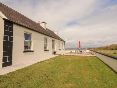 A grass yard with a patio table and chairs with a red umbrella outside a single story house at Newtown East near Kilkee County Clare