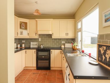 A kitchen with cream cabinets black countertops a black oven a stainless steel sink and a window at Newtown East near Kilkee County Clare