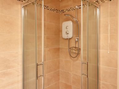 A shower enclosure with glass doors a wall-mounted shower unit and beige tiled walls at Newtown East near Kilkee County Clare