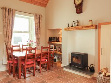 A dining area with wooden table and chairs near window and fireplace with wood stove at Newtown East near Kilkee County Clare