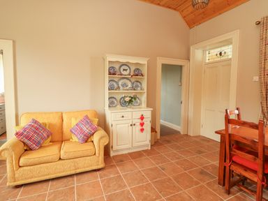 A room with a yellow sofa with colorful cushions a white cabinet with blue plates a wooden dining table and chairs at Newtown East near Kilkee County Clare
