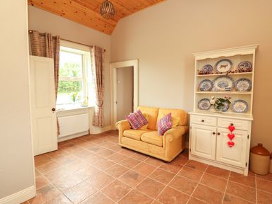 A living room with a yellow sofa two plaid pillows a cabinet with blue and white plates and a window with curtains at Newtown East near Kilkee County Clare