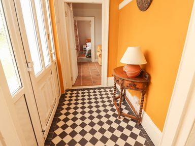 A hallway with checkered floor tiles an orange wall a small wooden table with a lamp and a view into a bedroom at Newtown East near Kilkee County Clare