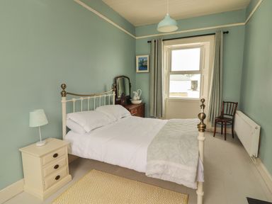 A bedroom with a bed side table with lamp a dresser with a mirror and window with curtains at Newtown East near Kilkee County Clare