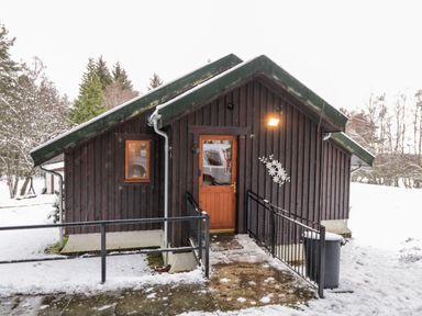 A wooden cabin with a ramp entrance and snow on the ground at Torbreck Chalet in Kincraig