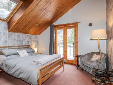 A bedroom with wooden bed frame and grey bedding under a wooden sloped ceiling at Torbreck Chalet in Kincraig