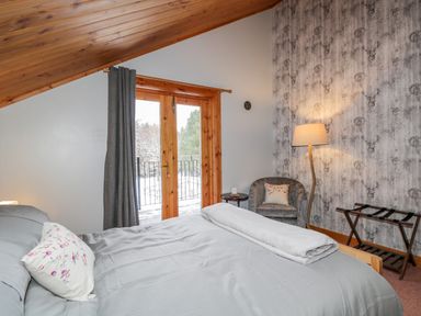 A bedroom with a bed a wooden ceiling a patterned wall a chair lamp and glass doors at Torbreck Chalet in Kincraig