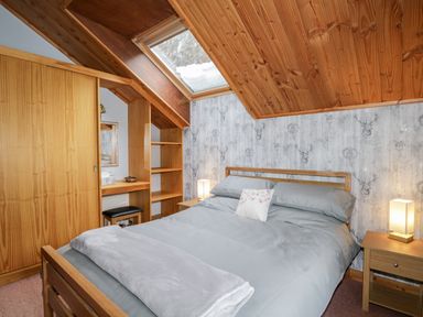 A bedroom with a wooden bed a bedside table with a lamp a built-in wooden wardrobe and shelving under a skylight at Torbreck Chalet in Kincraig