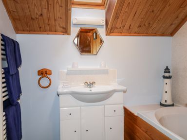 A bathroom with a white sink cabinet a hexagonal mirror wooden ceiling blue towels and a lighthouse decoration at Torbreck Chalet in Kincraig