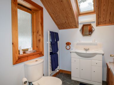 A bathroom with a toilet sink with cabinet towel rack and a window at Torbreck Chalet in Kincraig