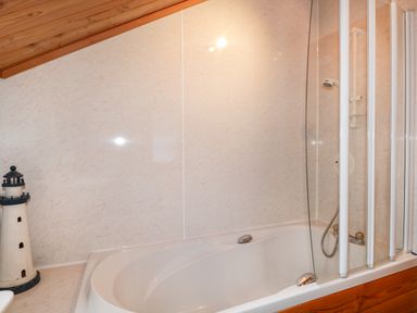 A bathroom with a white bathtub glass shower screen and a lighthouse decoration at Torbreck Chalet in Kincraig