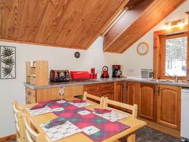 A kitchen with wooden cabinets a dining table set with placemats and napkins and a window showing a snowy landscape at Torbreck Chalet in Kincraig
