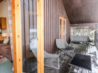 A balcony with chairs and a table next to a living room at Torbreck Chalet in Kincraig