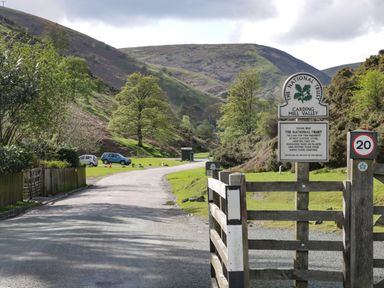 A road with parked cars and trees beside hills at Carding Mill Valley