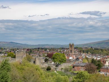 A town with a stone castle wall and a tall church tower surrounded by houses and trees at The Boars Head Pub in Bishop's Castle