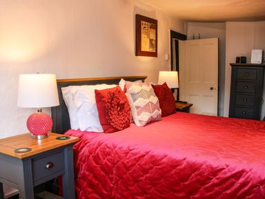 A bedroom with a bed covered in red bedding and decorative pillows two bedside tables with lamps and a black chest of drawers at The Boars Head Pub in Bishop's Castle