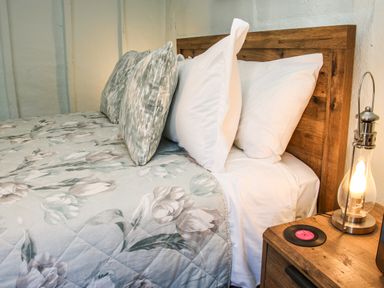 A bed with floral bedding and multiple pillows next to a wooden nightstand with a lamp and a small record at The Boars Head Pub in Bishops Castle
