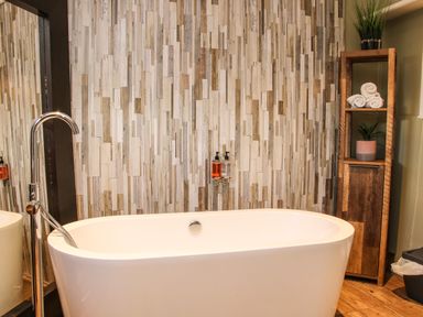 A bathroom with a freestanding bathtub a tall faucet a wooden shelving unit with towels and plants and a textured wooden wall at The Boars Head Pub in Bishop's Castle
