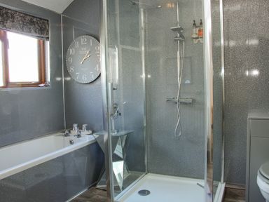 A bathroom with a bathtub a glass shower enclosure a clock on the wall and a window at The Boars Head Pub in Bishop's Castle