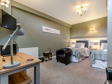 A bedroom with two single beds a black armchair a wooden desk with a lamp and a wall-mounted TV at The Boars Head Pub in Bishops Castle